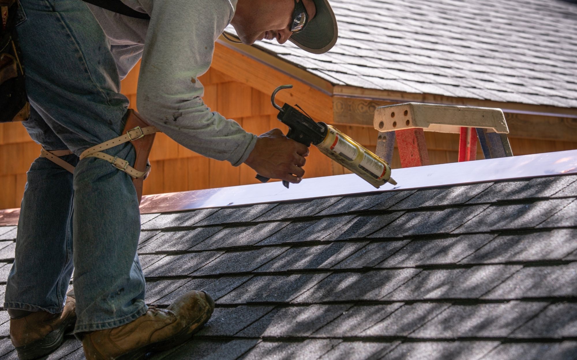 A man on a roof is using a caulking gun to fill in gaps in the shingles