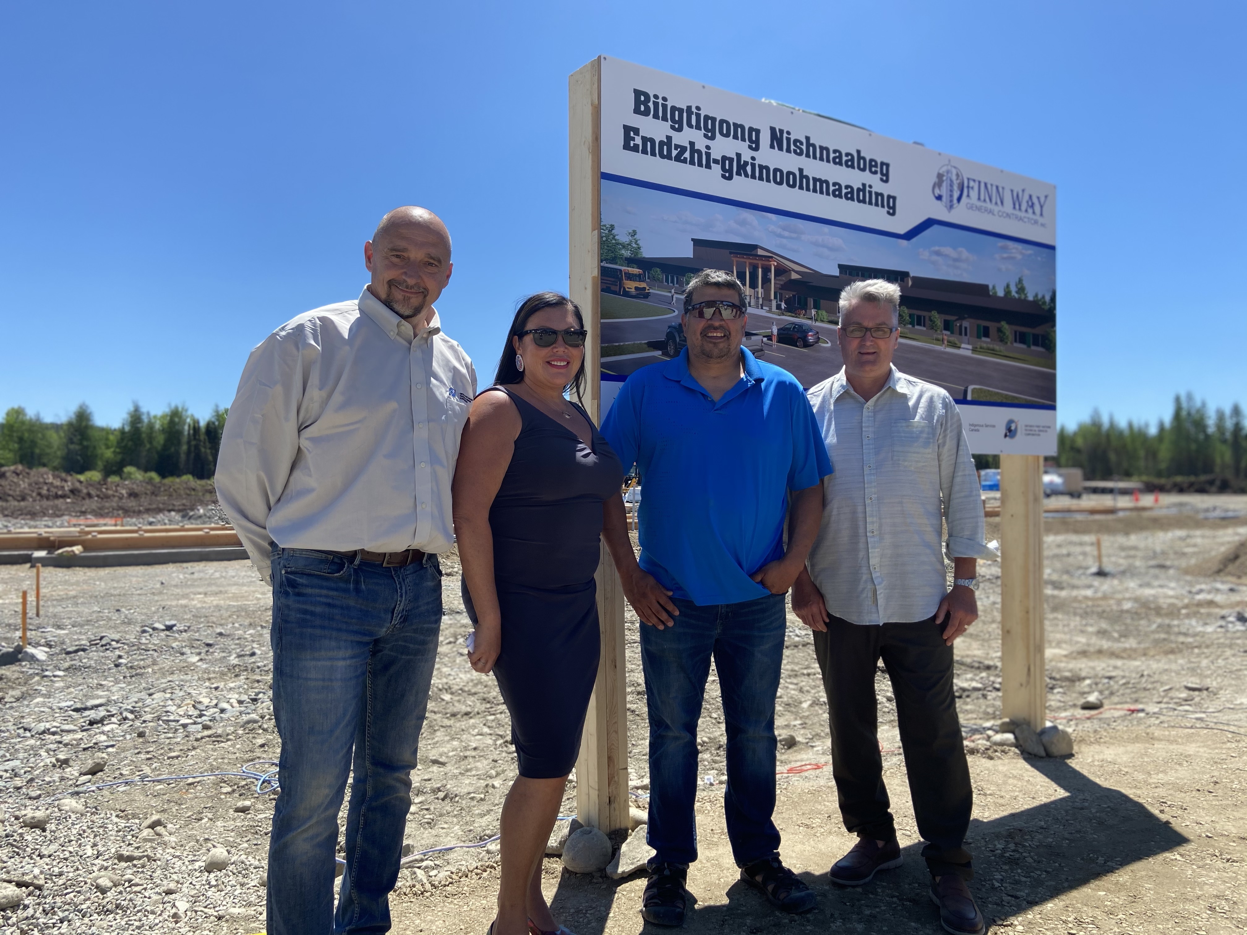 Darko Demitrijevic, Melanie Debassige, Daniel Michano and Glen Goodman stand in front of the construction site and sign for the new school