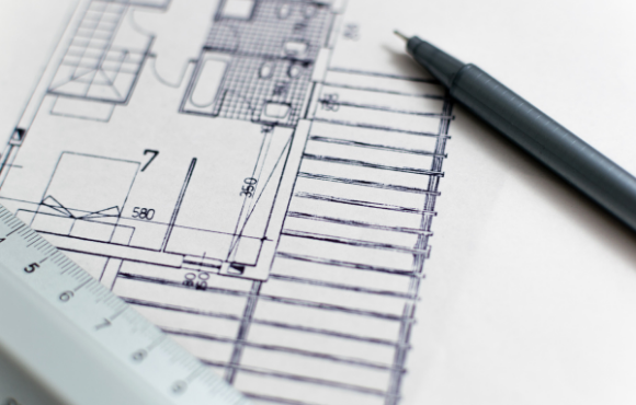 A close up of a pen laying diagonally on top of a blueprint for a house