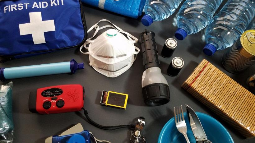 emergency items such as a mask, first aid kit, water bottles, matches, and more are splayed out on a table