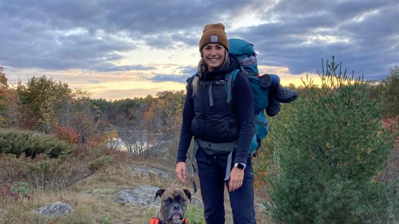 Madison is standing outside on a hiking trail in front of a cloudy sky with her dog.